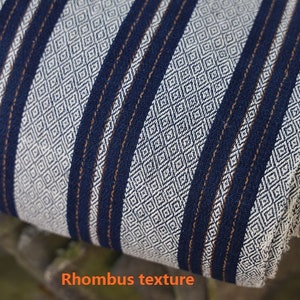 May include: Close-up of a white fabric with a blue and brown striped pattern. The fabric has a rhombus texture.