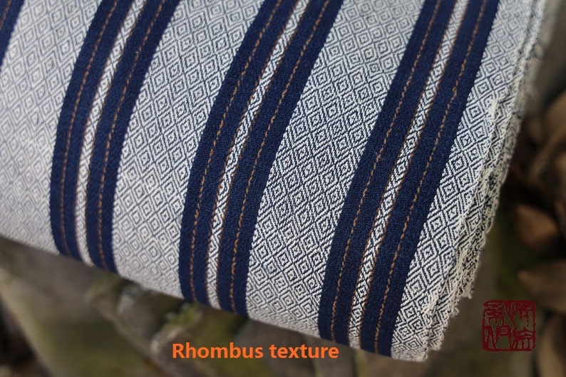 May include: Close-up of a white fabric with a blue and brown striped pattern. The fabric has a rhombus texture.