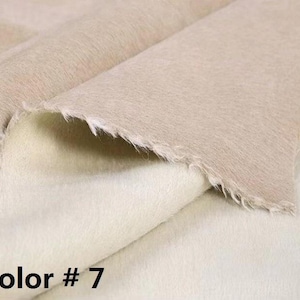 Peut inclure: Un morceau de tissu plié étiqueté Color # 7, présentant une surface extérieure beige clair lisse avec un tissage visible et une doublure intérieure blanc cassé douce et pelucheuse avec une texture duveteuse et des bords effilochés.