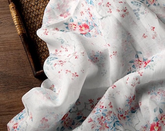 May include: A white fabric featuring a delicate floral pattern with small pink and red blossoms, light blue leaves, and thin gray branches. The material has a soft, slightly translucent texture with natural folds and gathers throughout the surface.