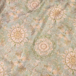 Pode incluir: Close-up de um tecido com um padrão floral repetido em tons de verde, bege e creme. O design apresenta grandes medalhões circulares com detalhes florais intrincados e pequenos detalhes florais espalhados.