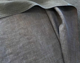 May include: A dark charcoal gray fabric with a visible woven texture. The material is folded over itself, creating soft, natural drapes and shadows that highlight the cross-hatched pattern of the weave across the surface of the textile.