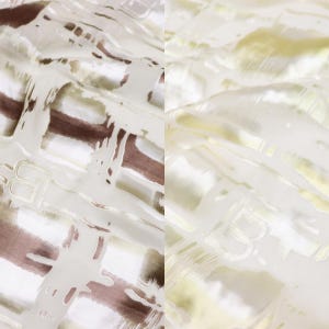 May include: Close-up of a fabric with a textured pattern. The fabric has a white base with brown and yellow brushstroke-like designs. The letter "B" is visible in the design. The fabric appears to be lightweight and possibly silk or a similar material.