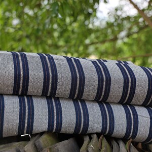 May include: Two rolls of striped fabric with blue and white stripes. The fabric is folded and stacked on top of each other. The fabric is on a wooden surface.