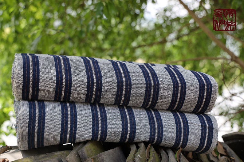 May include: Two rolls of striped fabric with blue and white stripes. The fabric is folded and stacked on top of each other. The fabric is on a wooden surface.