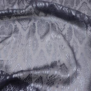 May include: A close-up of a sheer fabric with a snakeskin pattern. The fabric is a mix of gray and silver, with the pattern creating a textured effect. The light catches the fabric, highlighting the pattern.