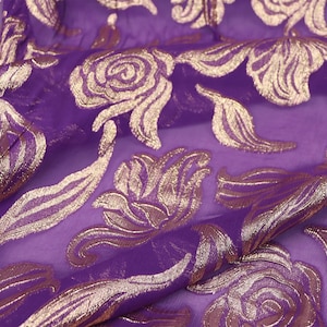 Puede incluir: Tela transparente púrpura con un patrón floral dorado. La tela es suave y fluida, y el patrón dorado es intrincado y detallado.