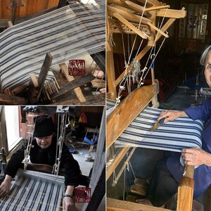 May include: A woman sits at a wooden loom, weaving a striped fabric. The loom is traditional and has a wooden frame with strings and a shuttle. The woman is wearing a blue shirt and black pants.
