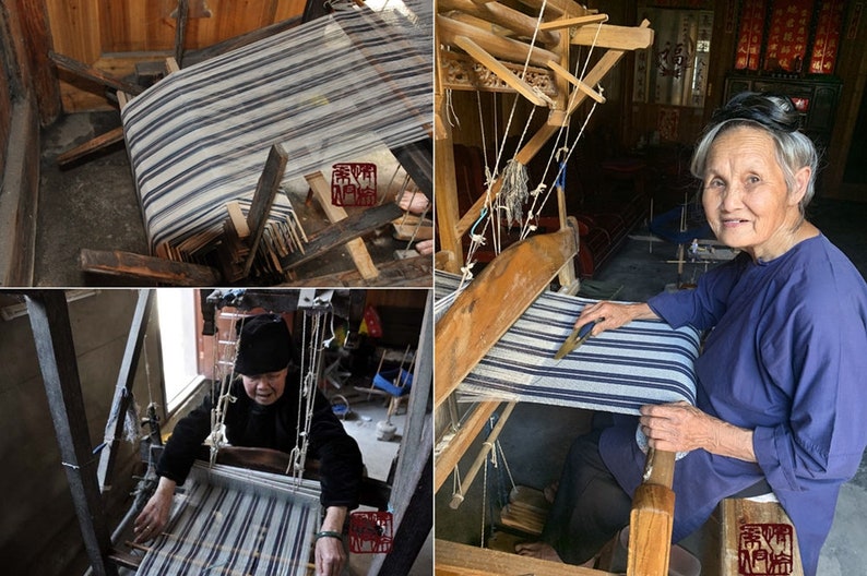 May include: A woman sits at a wooden loom, weaving a striped fabric. The loom is traditional and has a wooden frame with strings and a shuttle. The woman is wearing a blue shirt and black pants.