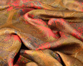 May include: A fabric textile featuring a vibrant red base color with an intricate, repeating pattern of golden-brown trees, leaves, and floral motifs. The material has a soft, draped texture with visible folds that create depth and shadows.