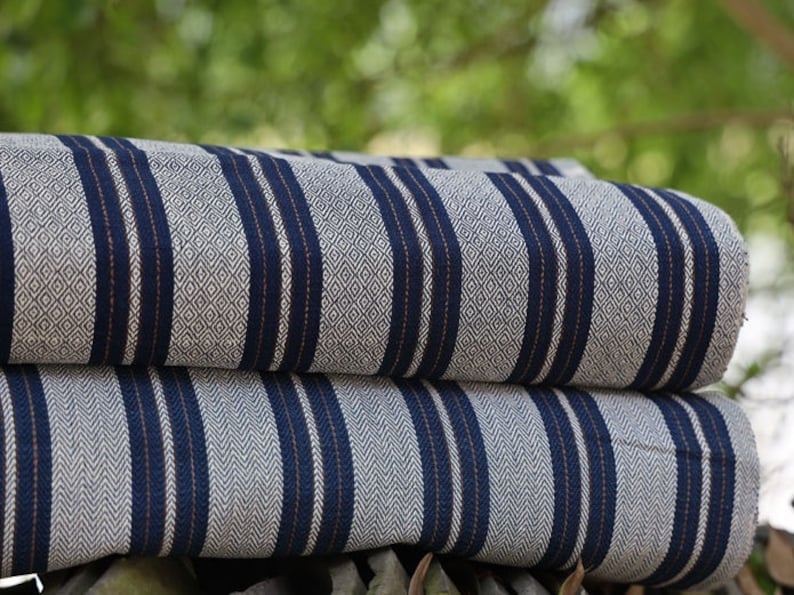 May include: Two pieces of striped fabric folded on top of each other. The fabric is white with blue and orange stripes. The stripes are woven into the fabric and have a diamond pattern.