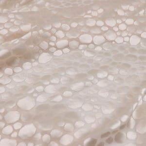 Puede incluir: Primer plano de una tela blanca con un patrón texturizado de círculos en relieve. La tela tiene un tacto suave y sedoso.