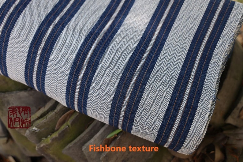 May include: White and blue striped fabric with a herringbone texture. The fabric has a subtle brown stripe running through it.