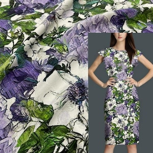 May include: Floral print fabric and a dress. The fabric features a pattern of purple, white, and green flowers and leaves on a white background. The dress has a similar floral pattern, with a round neckline and short sleeves. The dress is knee-length.
