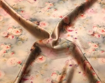 Pode incluir: Um tecido leve com uma estampa floral suave e desfocada, com grupos de rosas cor-de-rosa, creme e brancas espalhadas sobre um fundo pálido e neutro. O material está drapeado para mostrar dobras e uma textura de superfície lisa e levemente brilhante.