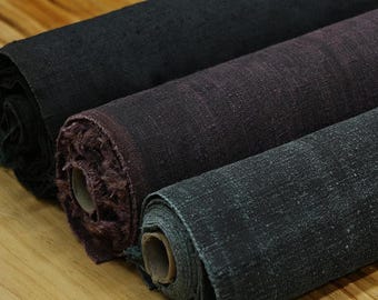 May include: Three rolls of fabric featuring a textured, woven appearance. The top roll is solid black, the middle roll is a deep plum purple, and the bottom roll is a dark charcoal gray. Each roll is wound around a central cardboard tube core.
