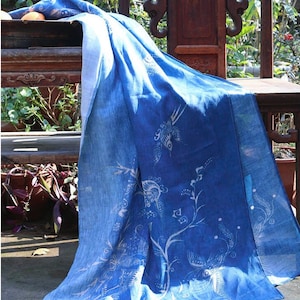 Puede incluir: Una manta de lino azul y blanco con un diseño chino tradicional. La manta está drapeada sobre una silla de madera con tallas intrincadas.