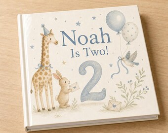 Puede incluir: Un libro de tapa dura cuadrado con una cubierta color crema que presenta una ilustración en acuarela de una jirafa con gorro de fiesta, un conejo sosteniendo un sobre, un pájaro, globos y el texto Noah Is Two! con un gran número 2 azul.
