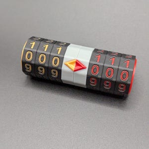 May include: A black combination lock with rotating number dials. The numbers are white and red, set against a black background. The lock has a gray center section with a red and yellow arrow-shaped design. The ends are red.