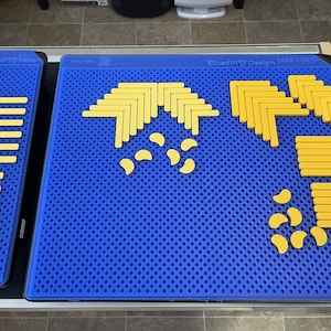 Op de afbeelding: Een blauw geperforeerd oppervlak met gele geometrische vormen erop. De vormen omvatten L-vormige stukken, rechte staven en halve manen. Links een kleiner blauw oppervlak met gele staven. De tekst "Sliced Ply Design" is zichtbaar.