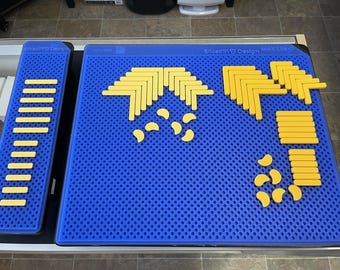 May include: A blue perforated surface with yellow geometric shapes arranged on it. The shapes include L-shaped pieces, straight bars, and crescent shapes. A smaller blue surface with yellow bars is to the left. The text "Sliced Ply Design" is visible.