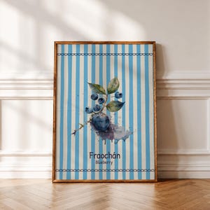 May include: A rectangular framed wall art print featuring a watercolor illustration of a blueberry branch with dark blue berries and green leaves. The background has vertical light blue and white stripes with scalloped borders. Text reads Fraochán Blueberry.