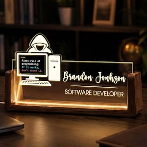 May include: A rectangular wooden desk sign with an illuminated acrylic panel featuring a hooded figure at a computer, the text "First rule of programming: If it works, don't touch it.", the name "Brandon Jonhson", and "SOFTWARE DEVELOPER".