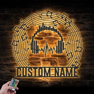 May include: A circular black metal wall sign featuring a central headphone icon with a sound wave graphic, surrounded by musical notes and staff lines. The sign is backlit with a warm glow and includes the text CUSTOM NAME at the bottom.