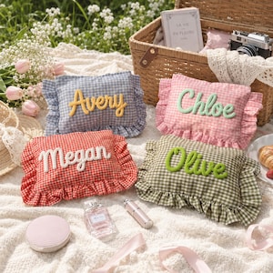May include: Four rectangular fabric pillows with ruffled edges and gingham patterns in blue, pink, red, and green. Each pillow features a personalized name in raised, cursive lettering: Avery in yellow, Chloe in light green, Megan in white, and Olive in bright green.