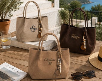 Könnte beinhalten: Drei Wildleder-Tragetaschen in Beige und Dunkelbraun, jeweils mit zwei Tragegriffen und einer dekorativen Perlenquaste. Die Taschen sind mit den Namen Sophia, Harper und Charlotte personalisiert, wobei neben Charlotte ein Schleifensymbol steht.