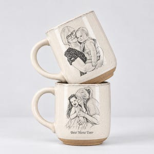 May include: Two speckled cream-colored ceramic mugs stacked vertically. The top mug features a black line drawing of an adult holding a baby. The bottom mug displays a black line drawing of an adult hugging a child with the text Best Nana Ever.