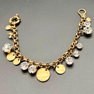 Op de afbeelding: Goudkleurige bedelarmband met een kettingontwerp met ronde schakels. De armband is versierd met heldere, ronde kristallen en kleine, goudkleurige schijfbedels. De sluiting is een eenvoudige haak- en oogsluiting.