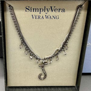 May include: A silver-toned necklace with a layered chain design and a pendant shaped like the letter "J". The necklace features small, clear crystal accents and is displayed in a branded box with the text "Simply Vera Vera Wang".