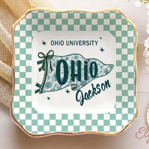May include: A square ceramic trinket dish with a gold rim and a checkered green and white border. The centre features a flag design with the text "OHIO UNIVERSITY" and "OHIO Jackson" in teal.