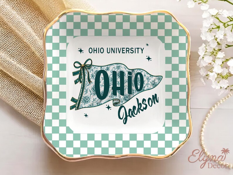 May include: A square ceramic trinket dish with a gold rim and a checkered green and white border. The centre features a flag design with the text "OHIO UNIVERSITY" and "OHIO Jackson" in teal.