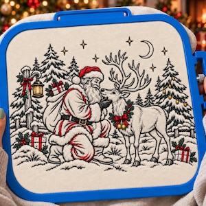 May include: A square blue embroidery hoop holding a fabric panel with a detailed black and white line art illustration of Santa Claus kneeling to greet a reindeer in a snowy forest setting with pine trees, gifts, a lantern, and a crescent moon.
