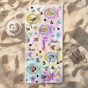 May include: A rectangular beach towel with a watercolor pastel background featuring various cartoon princess characters in ornate oval frames, small bows, red apples, and the word Name printed in purple. The towel is displayed on a sandy surface.