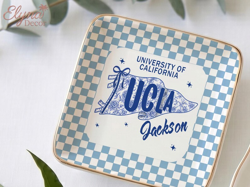 May include: Square ceramic tray with a light blue and white chequered pattern border and a gold rim. The centre features a UCLA banner design with the text "UNIVERSITY OF CALIFORNIA UCLA Jackson" in blue.