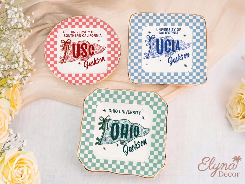 May include: Three decorative ceramic plates with university-themed designs. One is round with a red and white checkerboard pattern and "USC Jackson" text. Another is square with a blue and white checkerboard pattern and "UCLA Jackson" text. The third is square with a green and white checkerboard pattern and "OHIO Jackson" text.