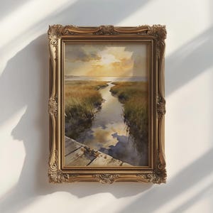 May include: A rectangular landscape painting in a decorative gold frame. The artwork depicts a narrow waterway flowing through grassy marshland toward a sunset horizon, with a wooden dock visible in the foreground reflecting the cloudy sky.
