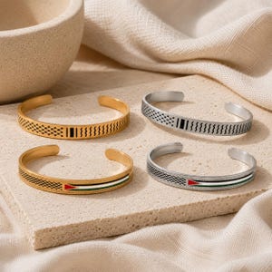 Pode incluir: Quatro pulseiras abertas em tons de ouro e prata. Duas pulseiras apresentam um padrão geométrico preto com linhas verticais. As outras duas pulseiras exibem um padrão geométrico preto ao lado de uma faixa horizontal com um design de bandeira nas cores vermelha, branca e verde.