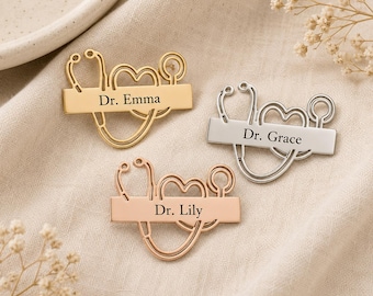 Può includere: Tre spille in metallo a forma di stetoscopio che forma un cuore, ognuna dotata di una barra orizzontale incisa con un nome. Le spille sono rifinite in tonalità oro, argento e oro rosa, con i nomi Dr. Emma, Dr. Grace e Dr. Lily incisi.
