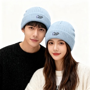 May include: Two people wearing light blue ribbed knit beanies with the word "GRAP" embroidered in black. The person on the left is wearing a black sweater, and the person on the right is wearing a white sweater.