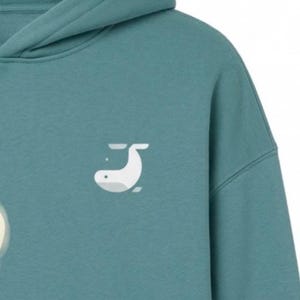 May include: Teal hoodie with a white whale graphic on the front. The hoodie has a hood and a relaxed fit. The whale graphic is a simple, minimalist design. The fabric appears to be a soft, comfortable material.
