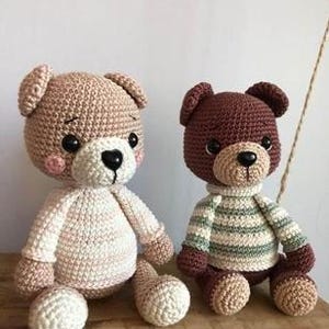 May include: Two crocheted teddy bears. One bear is light brown with a cream-colored belly and limbs. The other bear is dark brown and wears a green and cream striped sweater. Both have black eyes and black noses.