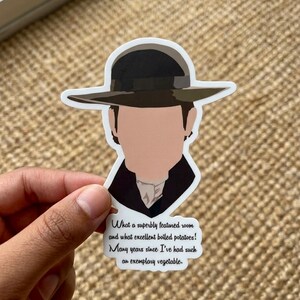 May include: A sticker featuring a faceless illustration of a person wearing a dark hat and coat. The sticker has text that reads, "What a superbly featured room and what excellent boiled potatoes! Many years since I've had such an exemplary vegetable."