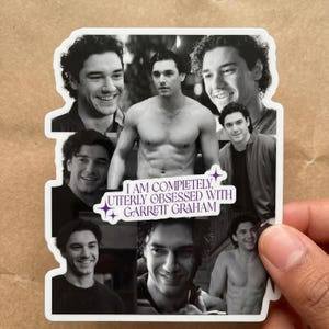 May include: A die-cut sticker featuring a collage of black and white photographs of a man with curly hair. In the center, a white rectangular label with purple text reads: I AM COMPLETELY, UTTERLY OBSESSED WITH GARRETT GRAHAM, accented by small stars.