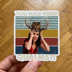 May include: A rectangular sticker featuring a person with a fox head and antlers resting on their head. The background consists of horizontal stripes in green, yellow, red, and blue. The text YOU HAD YOUR at the top and QUALMS?! at the bottom.