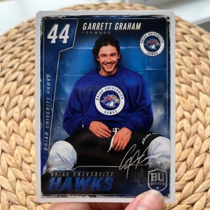 May include: A hockey trading card featuring Garrett Graham, a forward for Briar University Hawks. The card has a blue and white design with the number 44 prominently displayed. The Briar University Hawks logo is visible.