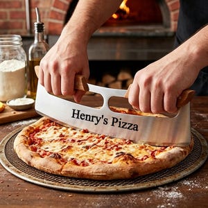 Könnte beinhalten: Ein Pizzaschneider mit Holzgriffen schneidet eine Pizza auf einem Metallblech. Die Pizza hat eine rote Soße und geschmolzenen Käse. Der Text "Henry's Pizza" ist auf der Klinge des Schneiders eingraviert.